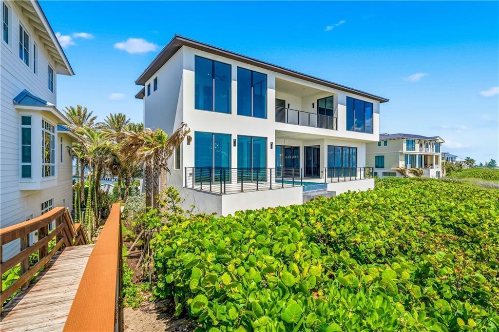 A modern white two-story house features large glass windows, a balcony, and a pool deck — JENSEN BEACH, FL