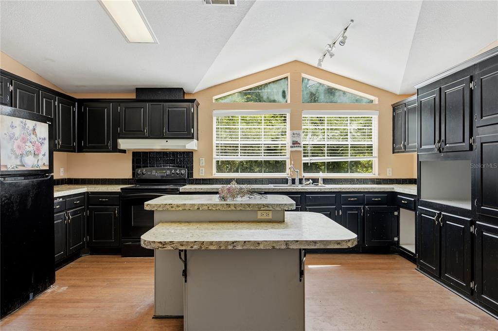 A kitchen features black cabinets, a two-tiered island, light countertops, and vaulted ceilings with windows — 819 LENORE AVENUE, INTERLACHEN, FL
