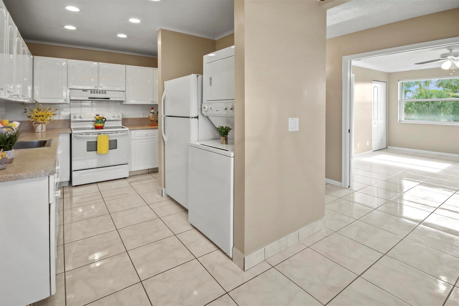 A kitchen with white cabinets and appliances features a stacked washer and dryer unit — 1421 NW 20th Avenue # 204, Delray Beach FL 33445, DELRAY BEACH, FL