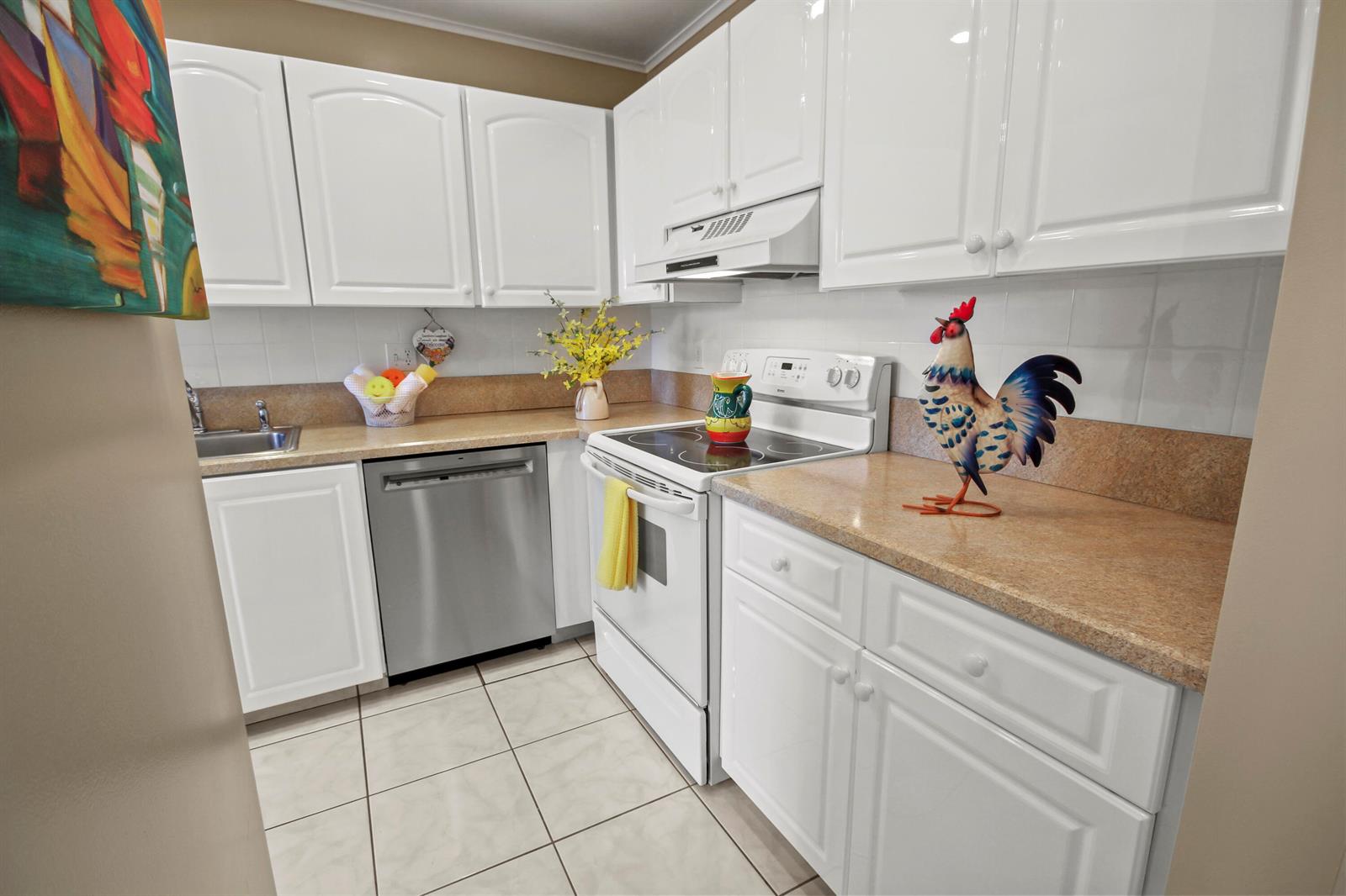 A kitchen features white cabinets, stainless steel appliances, tan countertops, and a decorative rooster figurine — 1421 NW 20th Avenue # 204, Delray Beach FL 33445, DELRAY BEACH, FL