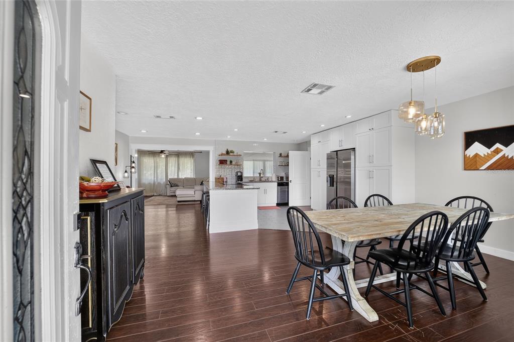 An open-concept dining area and kitchen featuring wood flooring, white cabinetry, and a rustic table — 1428 SE 9TH AVENUE, OCALA, FL