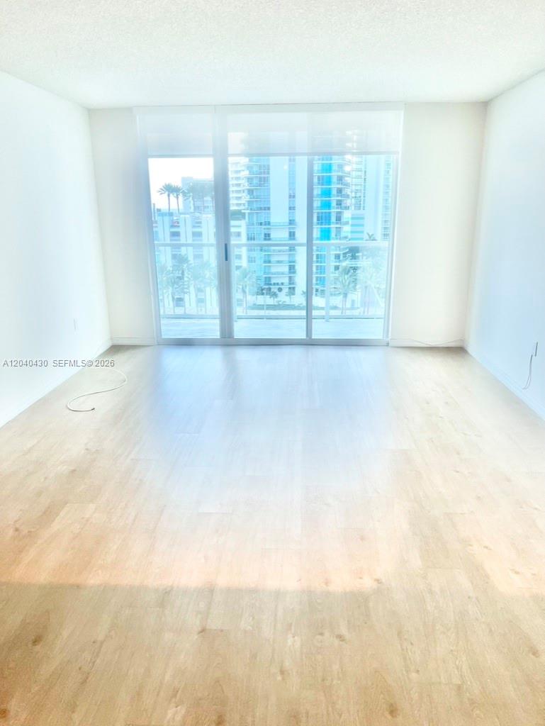 An empty room features light wood-look flooring, white walls, and a large sliding glass door — 1155 BRICKELL BAY DR # 807, Miami FL 33131, MIAMI, FL