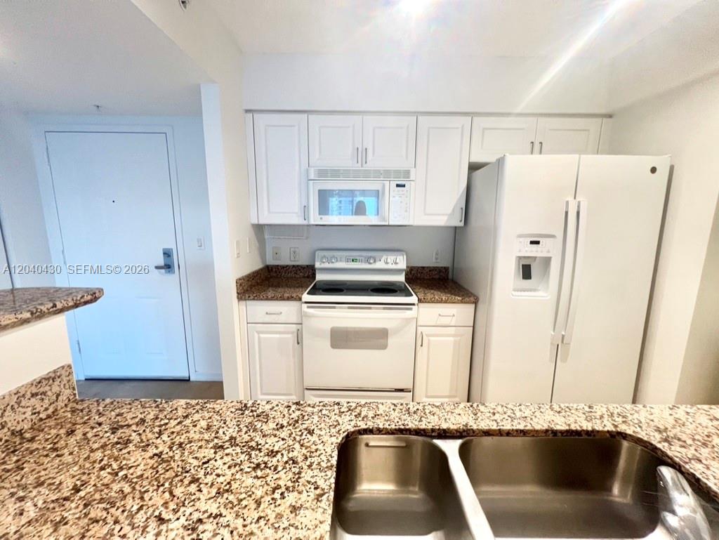 A kitchen features white cabinetry, granite countertops, and white appliances — 1155 BRICKELL BAY DR # 807, Miami FL 33131, MIAMI, FL