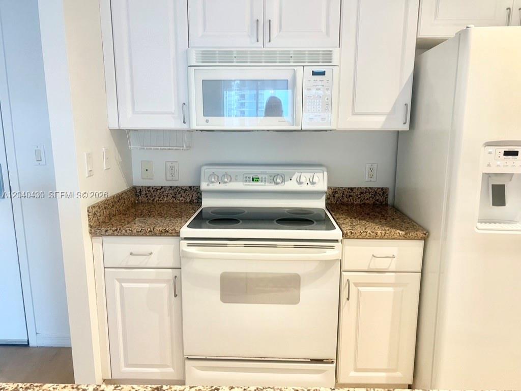 A kitchen features white cabinets, a white electric range, a microwave, and granite countertops — 1155 BRICKELL BAY DR # 807, Miami FL 33131, MIAMI, FL
