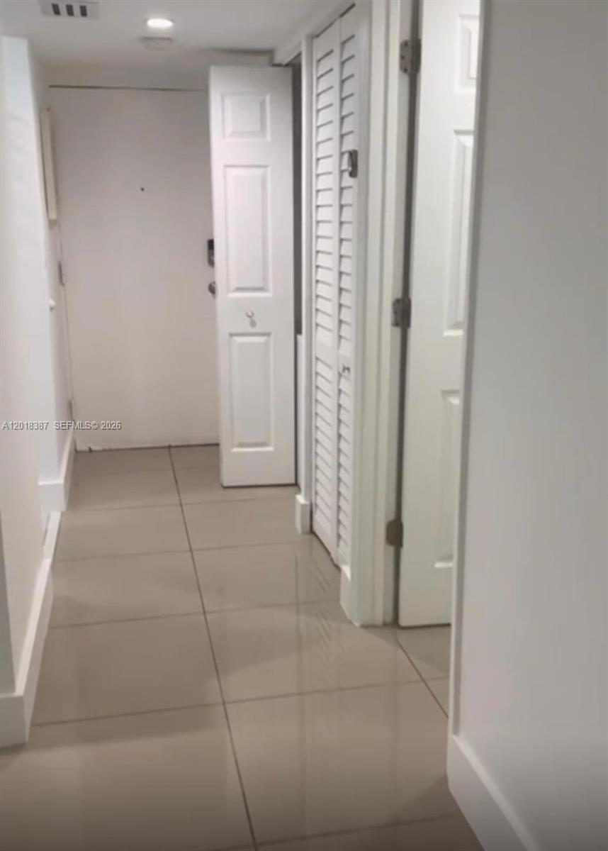A hallway with light-colored tile flooring leads to a white door and closet doors — 8004 SW 149th Ave # C418, Miami FL 33193, MIAMI, FL