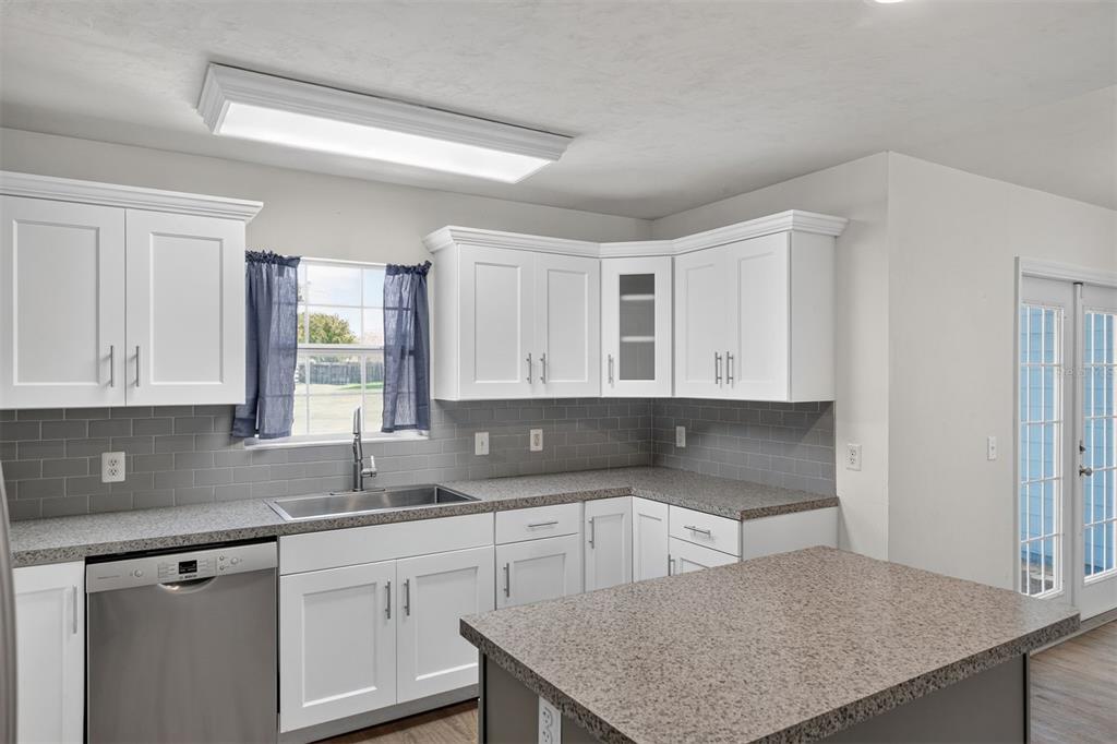 A kitchen features white cabinets, gray subway tile backsplash, speckled countertops, and a center island — 9892 SW 95TH PLACE, GAINESVILLE, FL