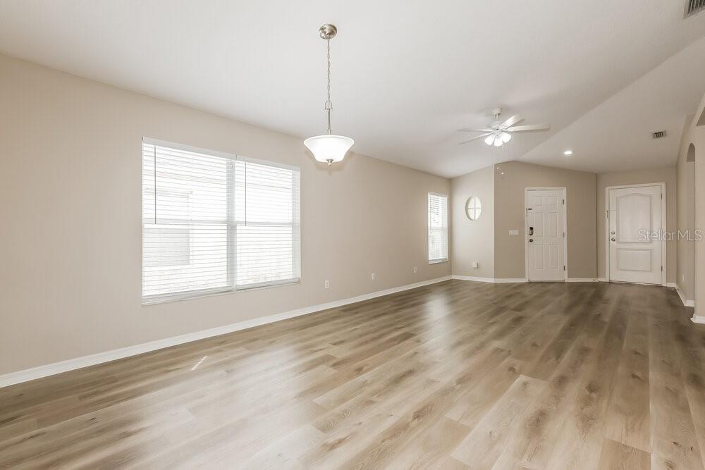 An empty room features light wood-look flooring, beige walls, a ceiling fan, and a chandelier — 1038 HARVEST MOON DRIVE, SEFFNER, FL