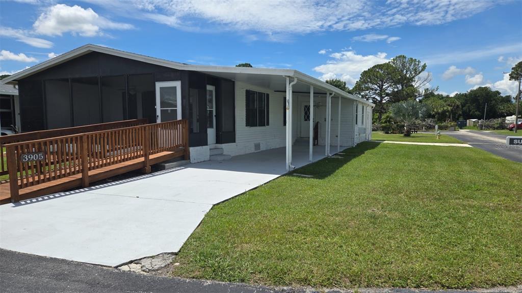 A single-story manufactured home features a screened-in porch, a wooden wheelchair ramp, and a carport — 3905 SUGAR BERRY PLACE, COCOA, FL