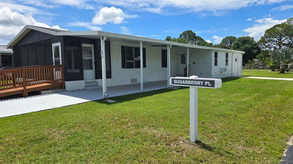 A single-story mobile home with a white exterior, a carport, and a wooden wheelchair ramp — 3905 SUGAR BERRY PLACE, COCOA, FL