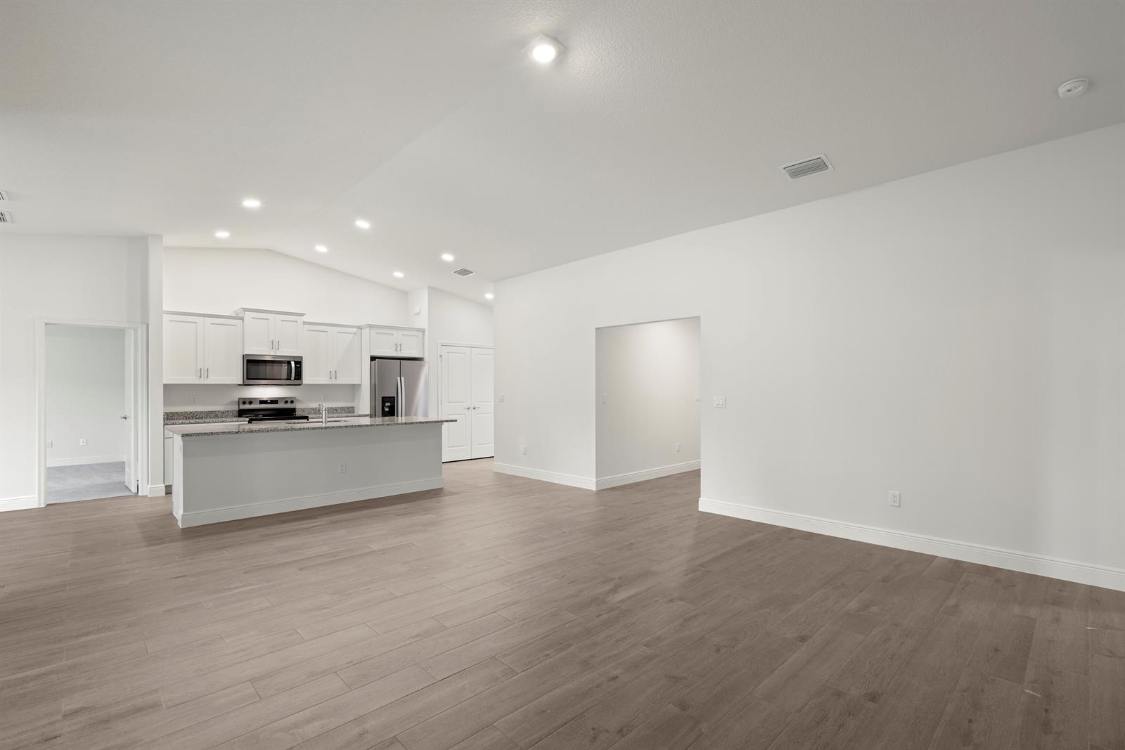 An open-concept kitchen with white cabinets and an island overlooks a spacious living area — 16227 69th Street N, Loxahatchee FL 33470, LOXAHATCHEE, FL