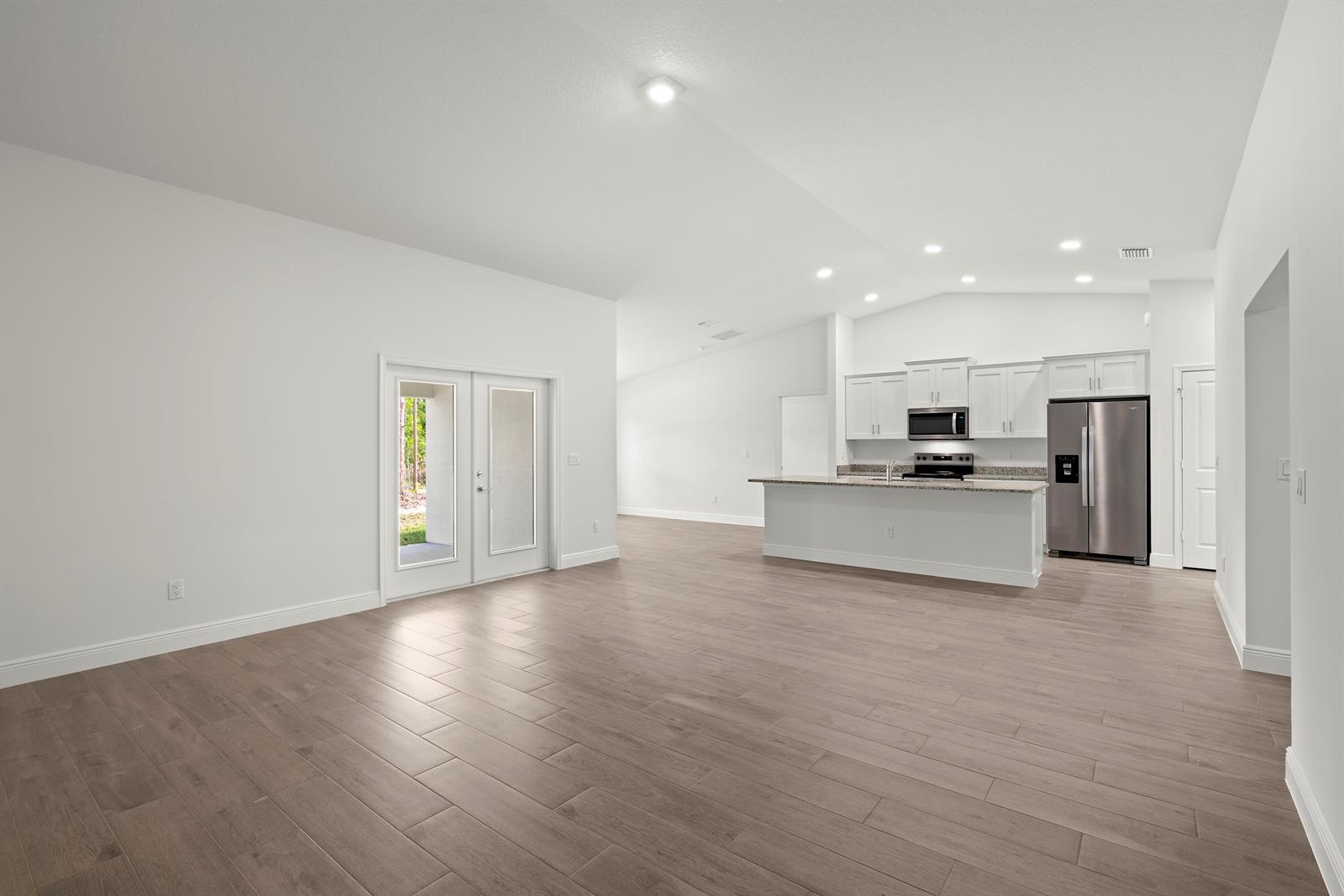 An open-concept living area features light wood-look tile flooring, white walls, and a modern kitchen — 16227 69th Street N, Loxahatchee FL 33470, LOXAHATCHEE, FL