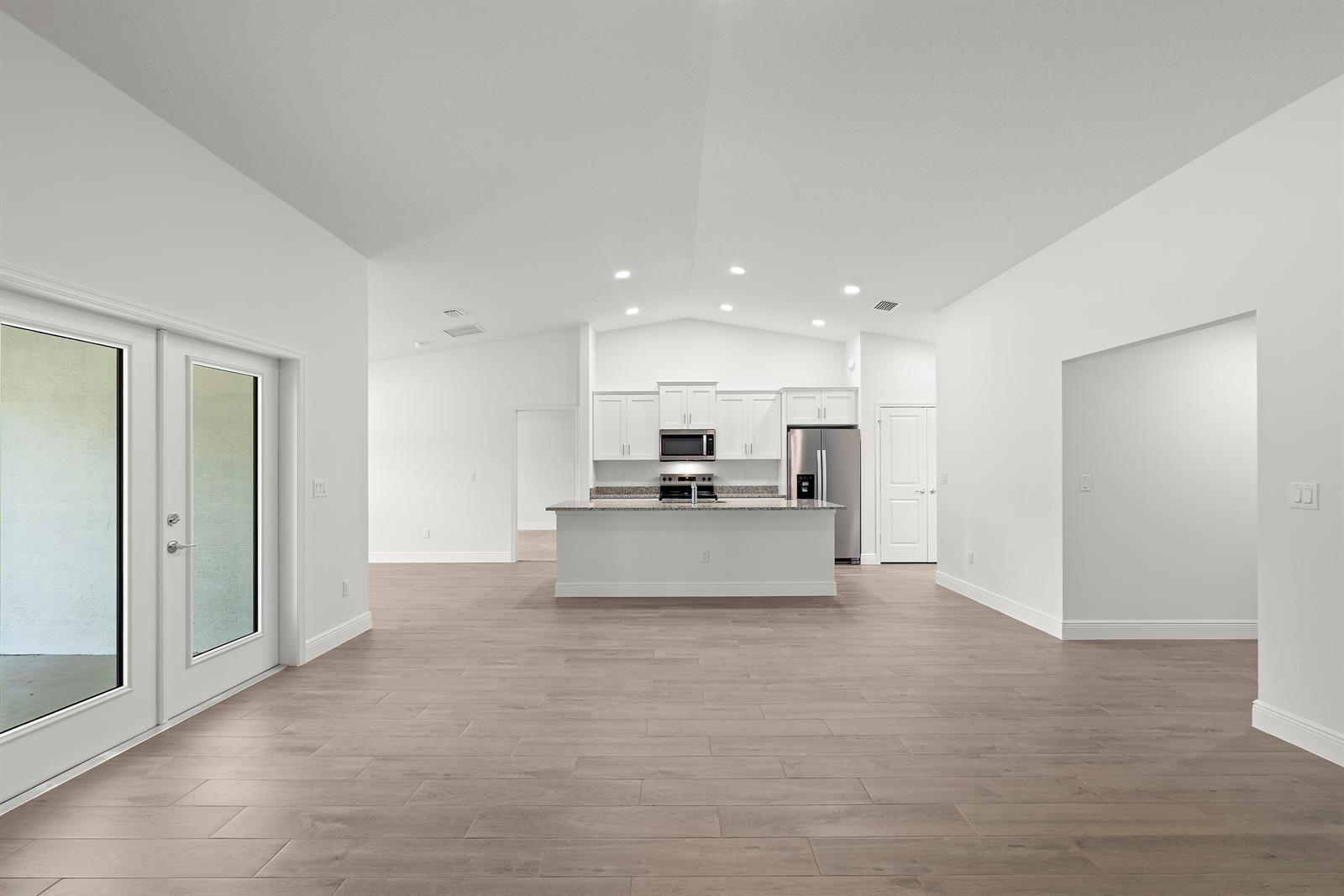 A bright, open-concept kitchen features white cabinetry, stainless steel appliances, and wood-look tile flooring — 16227 69th Street N, Loxahatchee FL 33470, LOXAHATCHEE, FL