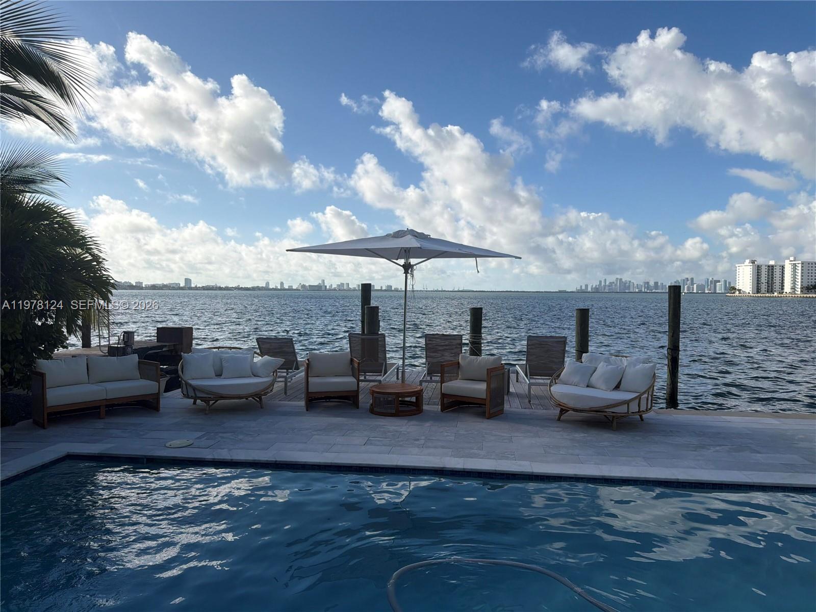 A swimming pool overlooks a wooden deck with outdoor furniture and a bay view — 1930 Bay Dr # 4, Miami Beach FL 33141, MIAMI BEACH, FL