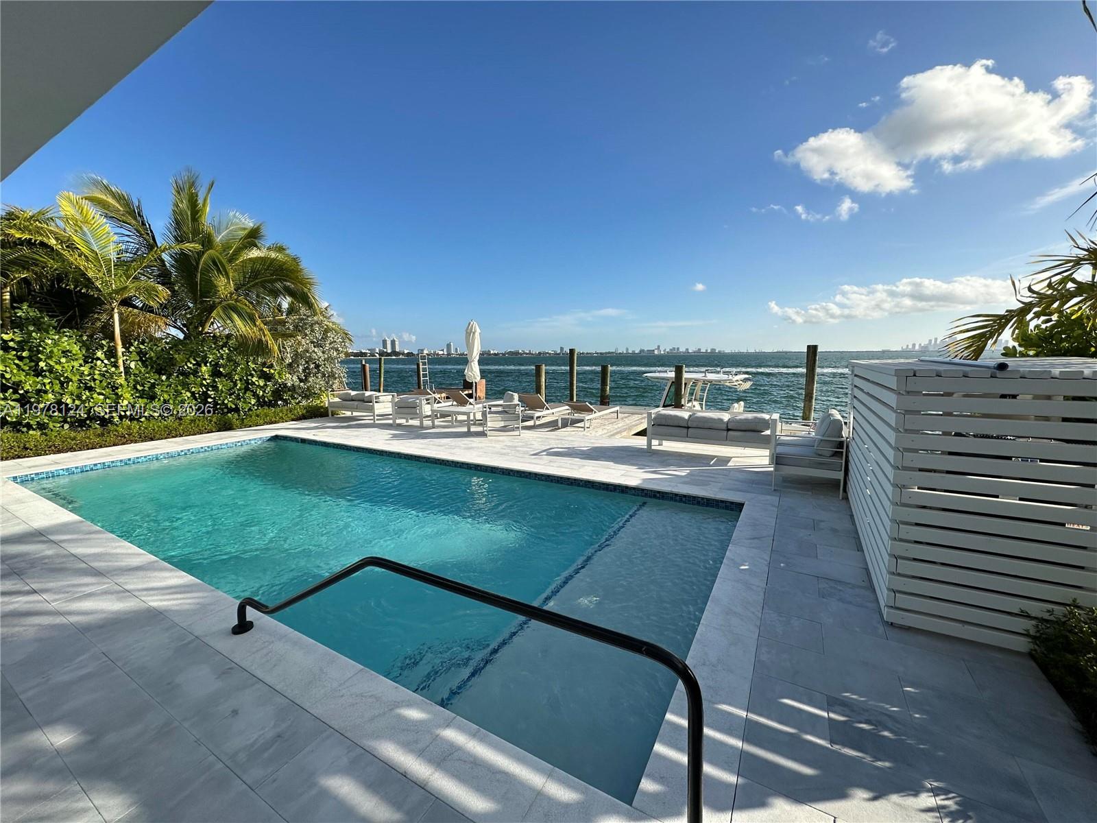 A swimming pool with a black handrail overlooks a bay with a distant city skyline — 1930 Bay Dr # 4, Miami Beach FL 33141, MIAMI BEACH, FL