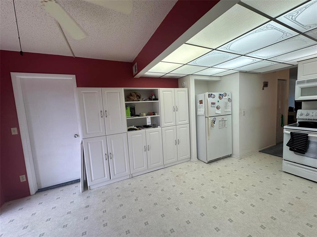 A kitchen features white cabinetry, a white refrigerator, and a drop ceiling with fluorescent lighting — 5090 BAY STREET NE UNIT 220, ST PETERSBURG, FL