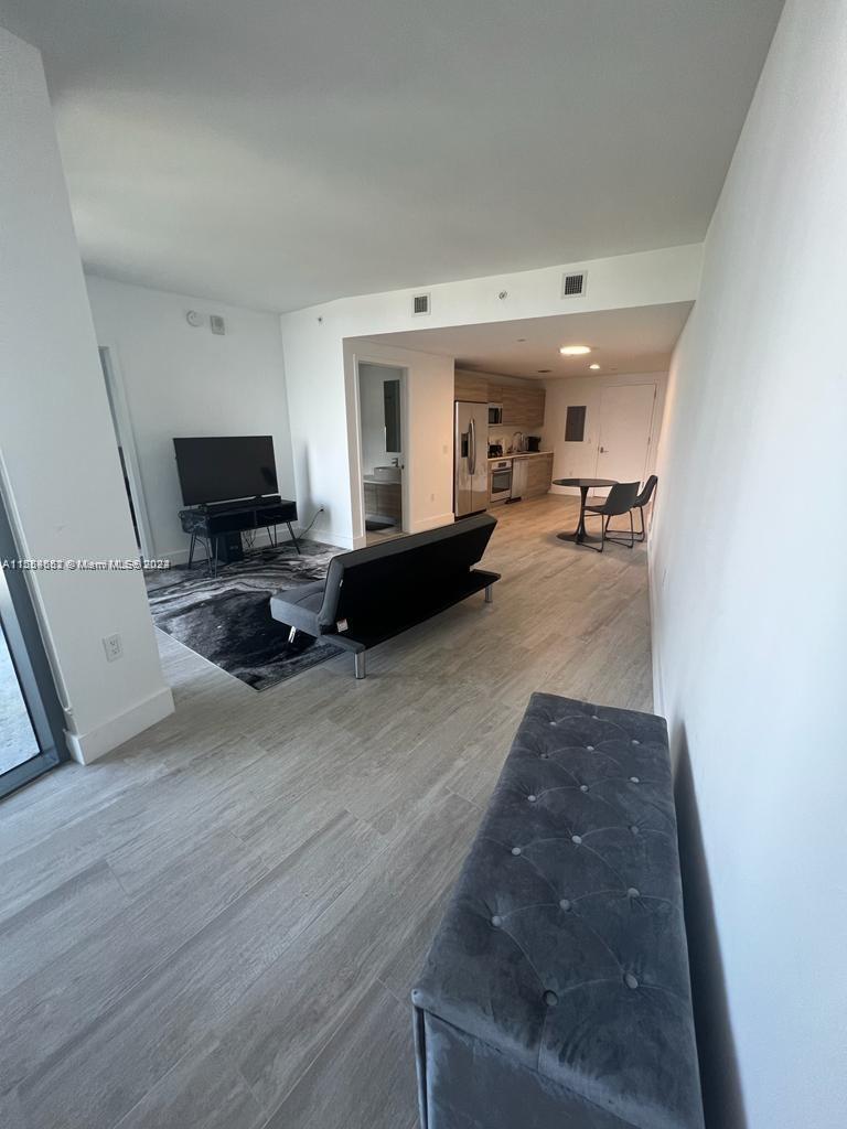An open-concept living area features light wood-look flooring, a kitchen, and a gray sofa — 121 NE 34th St # 2014, Miami FL 33137, MIAMI, FL