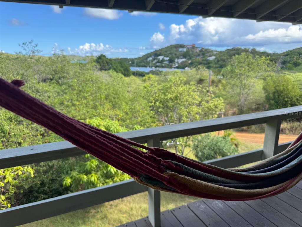 A colorful hammock hangs on a wooden deck overlooking a lush landscape and distant bay — 4 BARRIO PLAYA SARDINAS, CULEBRA, PR