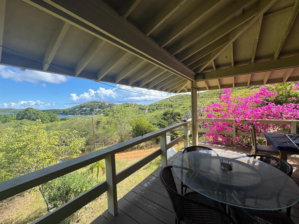 A covered wooden deck features a glass-top dining table overlooking a lush, hilly landscape — 4 BARRIO PLAYA SARDINAS, CULEBRA, PR