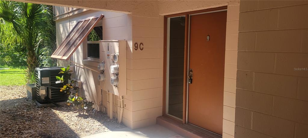 The exterior view shows a tan building entrance labeled 9C with an adjacent air conditioner — 180 MAGNOLIA WOODS COURT UNIT 9C, DELTONA, FL