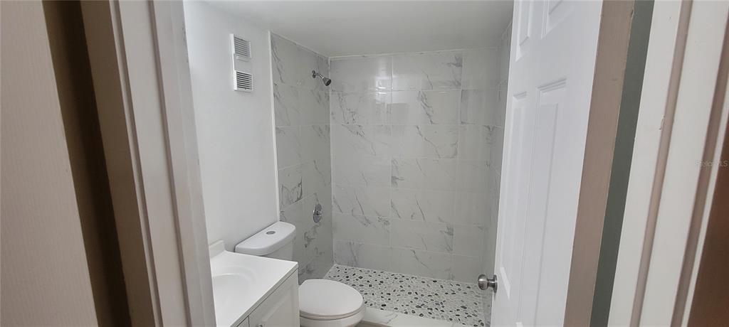 A small bathroom features a white vanity, a toilet, and a walk-in shower with marble-look tiles — 180 MAGNOLIA WOODS COURT UNIT 9C, DELTONA, FL