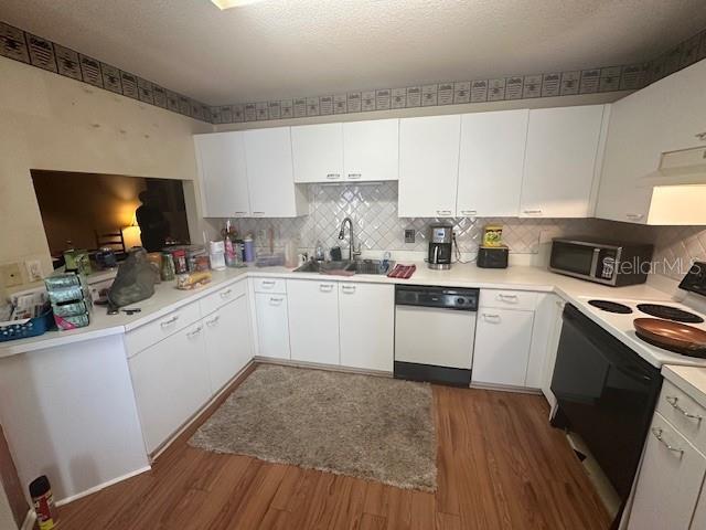 A kitchen features white cabinetry, a black dishwasher, a microwave, and wood-look flooring — 5445 18TH COURT W, BRADENTON, FL