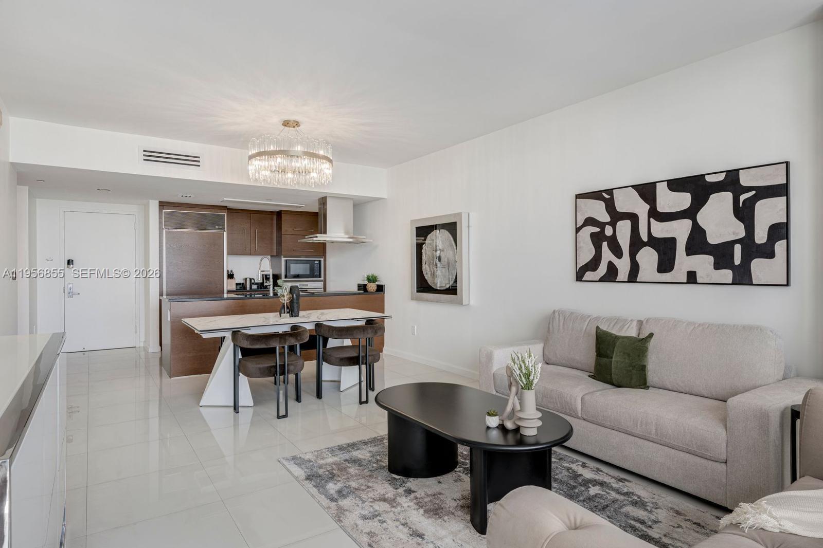 A modern open-concept living and dining area features a kitchen, chandelier, and neutral furniture — 485 Brickell Ave # 4706, Miami FL 33131, MIAMI, FL