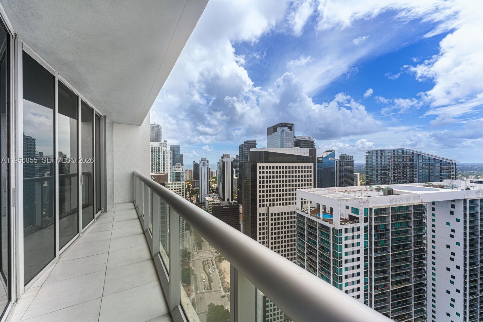 A high-rise balcony with tiled flooring overlooks a dense city skyline under a cloudy sky — 485 Brickell Ave # 4706, Miami FL 33131, MIAMI, FL