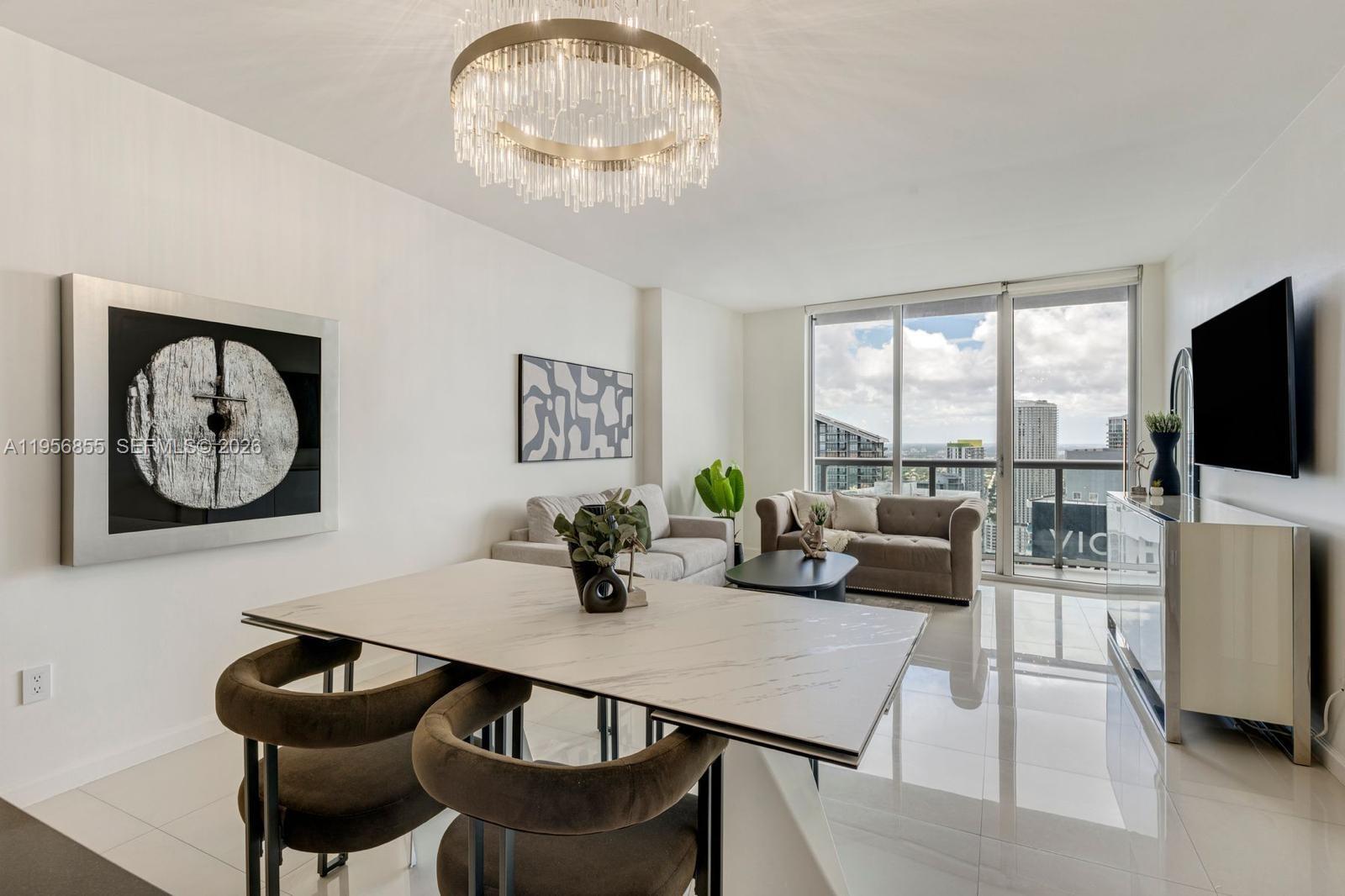 A modern living and dining area features a marble table, chandelier, and floor-to-ceiling windows — 485 Brickell Ave # 4706, Miami FL 33131, MIAMI, FL