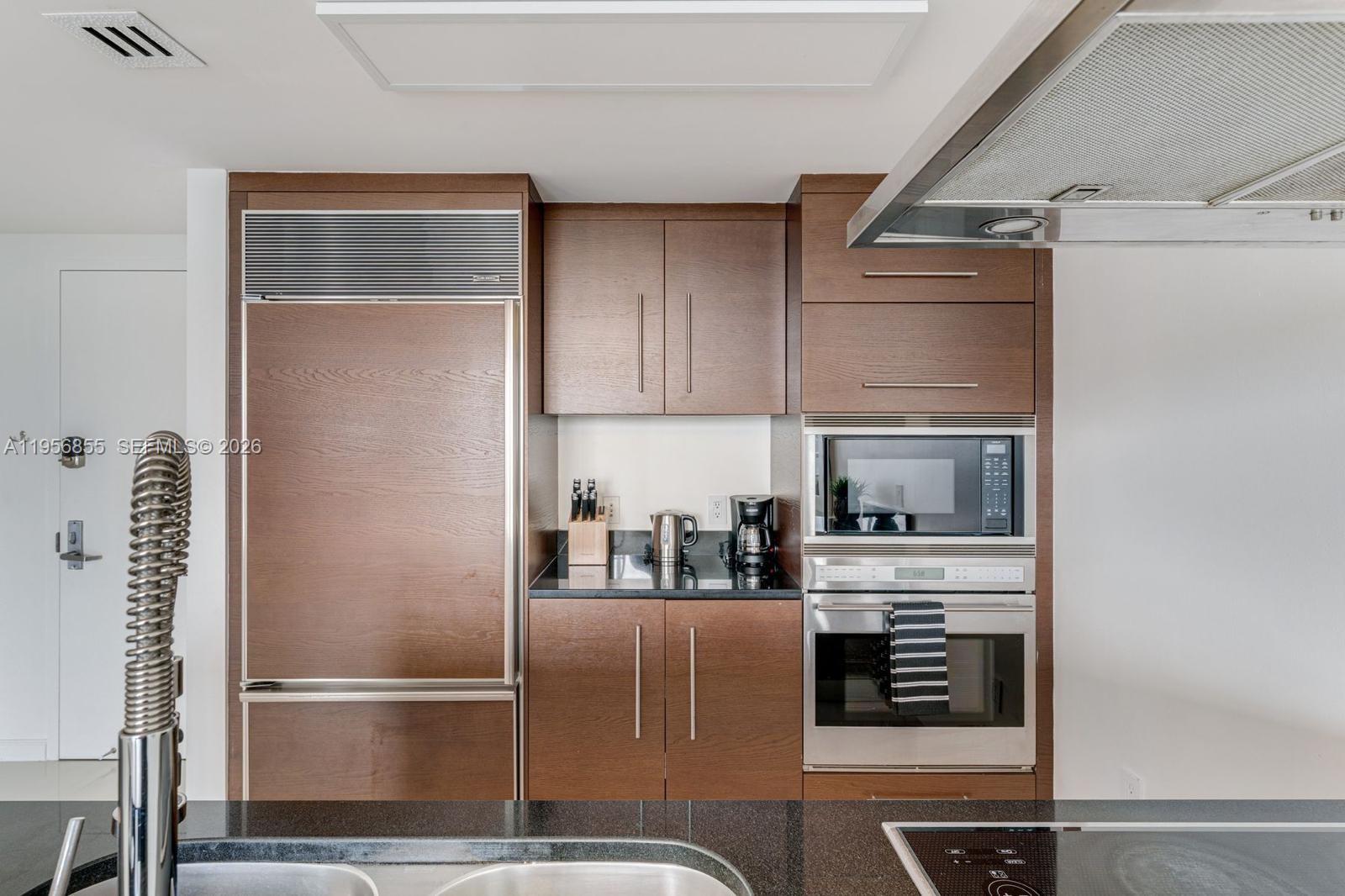 A modern kitchen features wood cabinetry, stainless steel appliances, and black granite countertops — 485 Brickell Ave # 4706, Miami FL 33131, MIAMI, FL