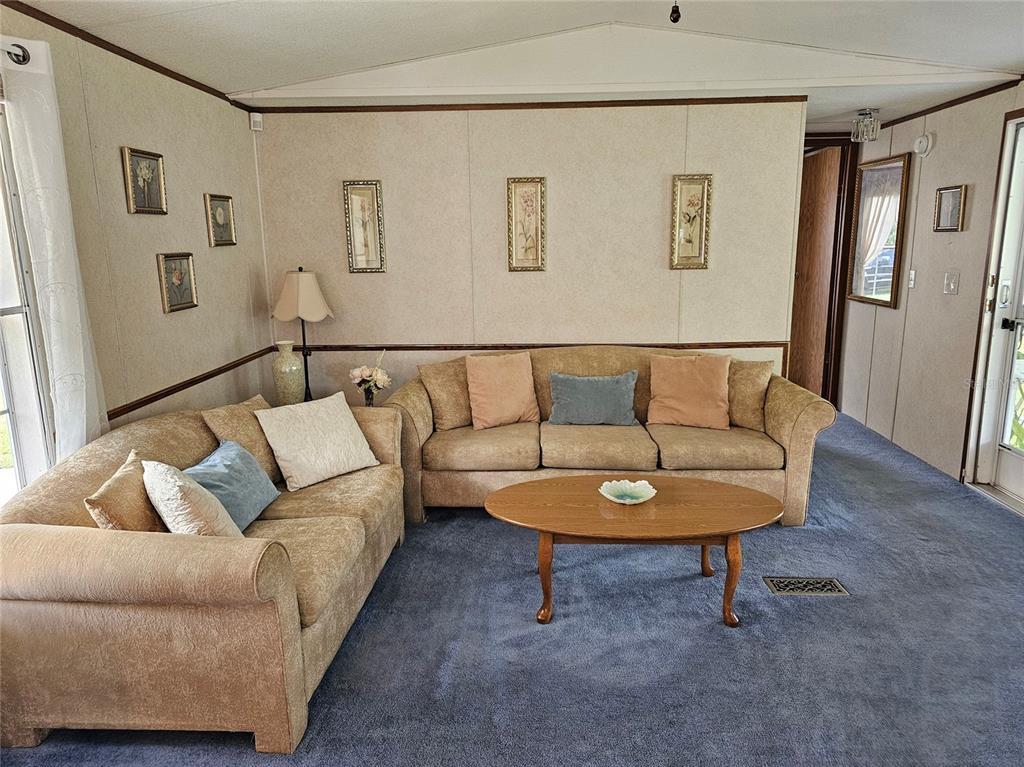 A living room features tan sofas, a wooden coffee table, and blue carpeted flooring — 1340 SAWDUST TRAIL, KISSIMMEE, FL