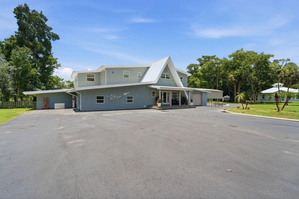 A large, light-green two-story house with a metal roof sits behind a wide asphalt driveway — 220 BRANDY COURT, DELTONA, FL