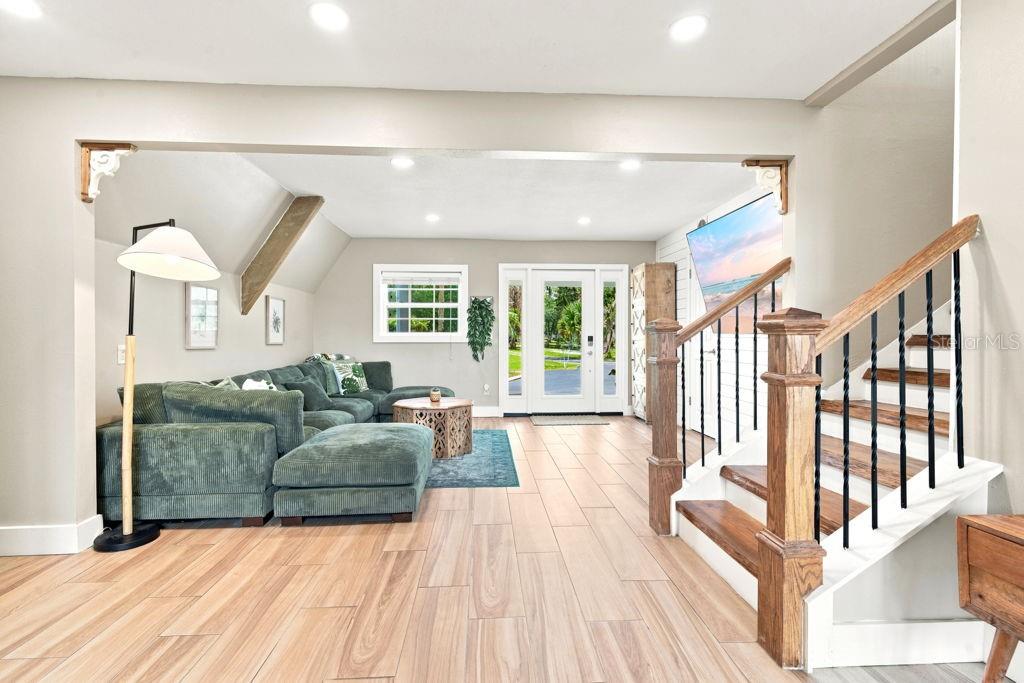 A living room features a green sectional sofa, wood-look tile flooring, and a wooden staircase — 220 BRANDY COURT, DELTONA, FL