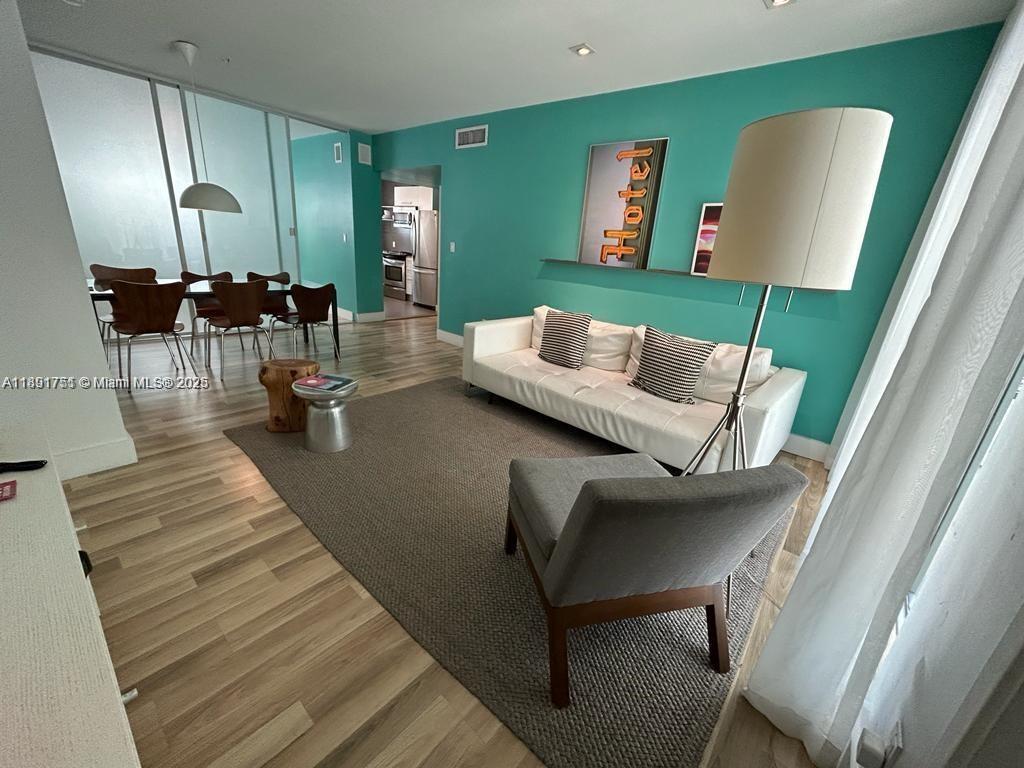 A living and dining area features teal walls, wood-look flooring, and a white sofa — 1816 Meridian Ave # 18, Miami Beach FL 33139, MIAMI BEACH, FL