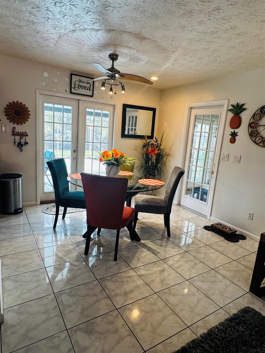 A dining area features a glass table, four colorful chairs, tile flooring, and two glass doors — 1918 SE Monroe Street, Stuart FL 34997, STUART, FL