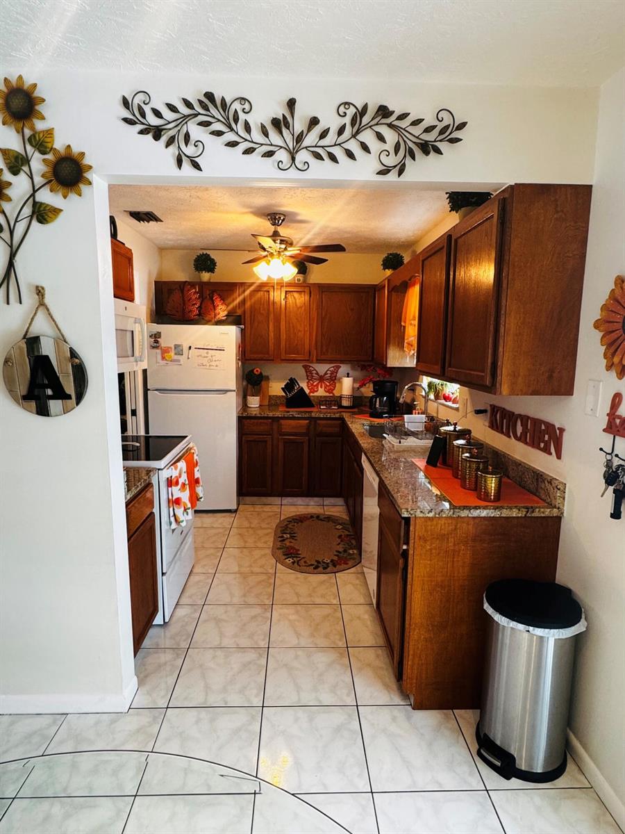 A galley-style kitchen features wood cabinets, granite countertops, tile flooring, and a ceiling fan — 1918 SE Monroe Street, Stuart FL 34997, STUART, FL