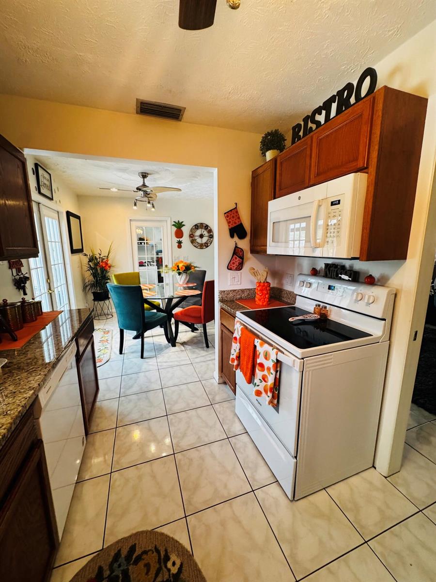 A kitchen with white appliances and wood cabinets leads into a dining area with colorful chairs — 1918 SE Monroe Street, Stuart FL 34997, STUART, FL
