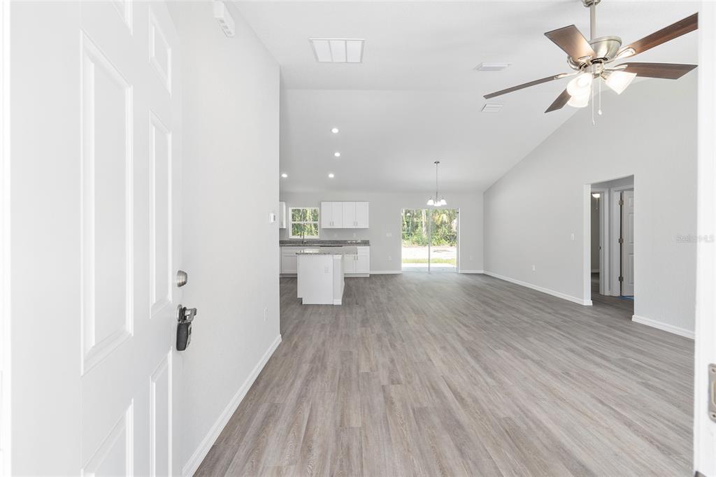 An open-concept living area with light wood-look flooring, a kitchen island, and a ceiling fan — 202 FISHER LOOP, OCKLAWAHA, FL