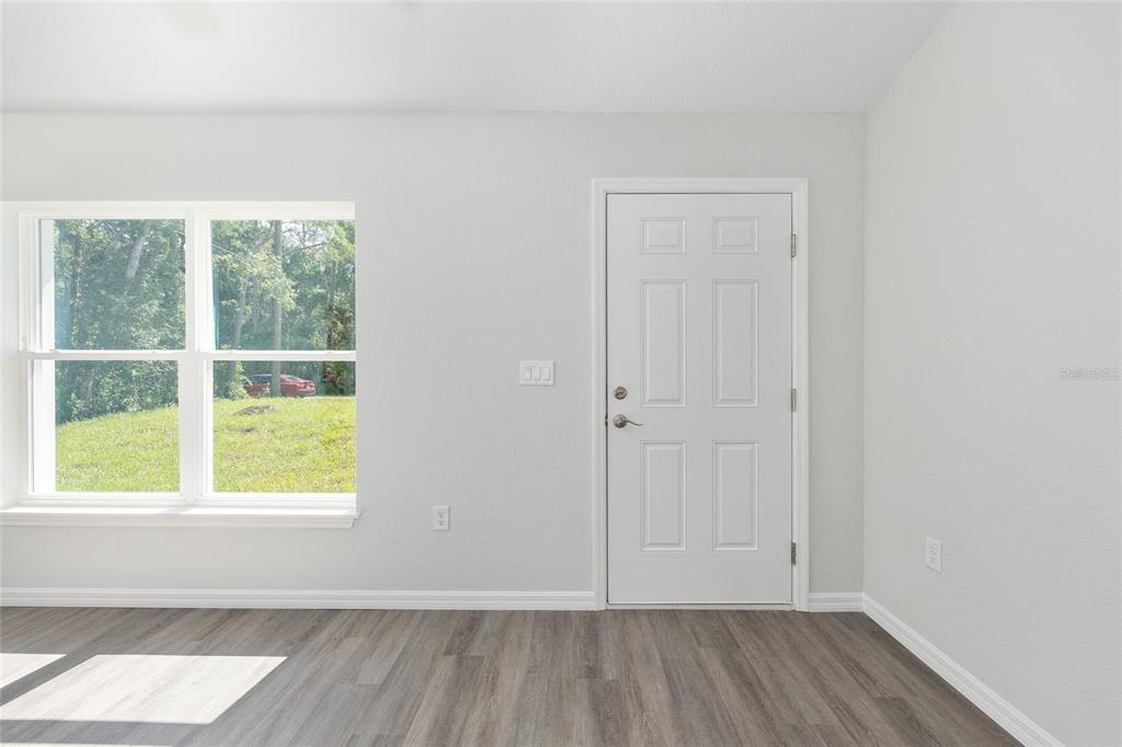 A room with light gray walls, wood-look flooring, a window, and a white entry door — 202 FISHER LOOP, OCKLAWAHA, FL