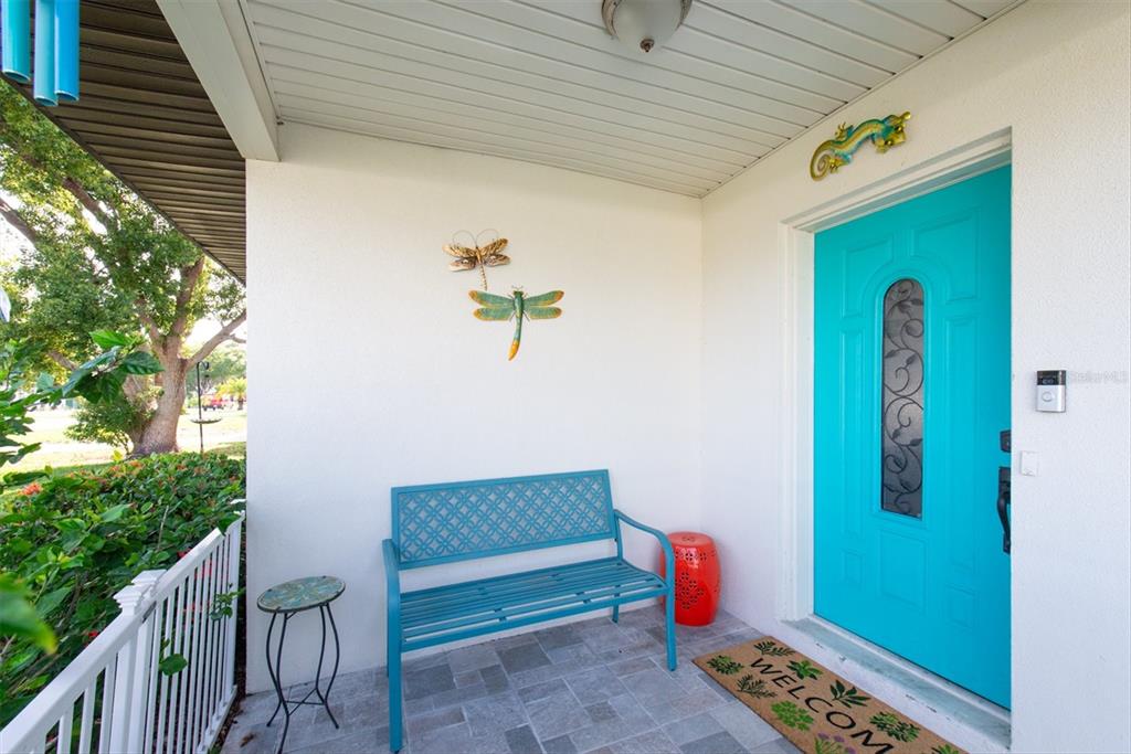 A front porch features a bright turquoise door, a matching metal bench, and dragonfly wall decor — 1468 LEMON STREET, CLEARWATER, FL