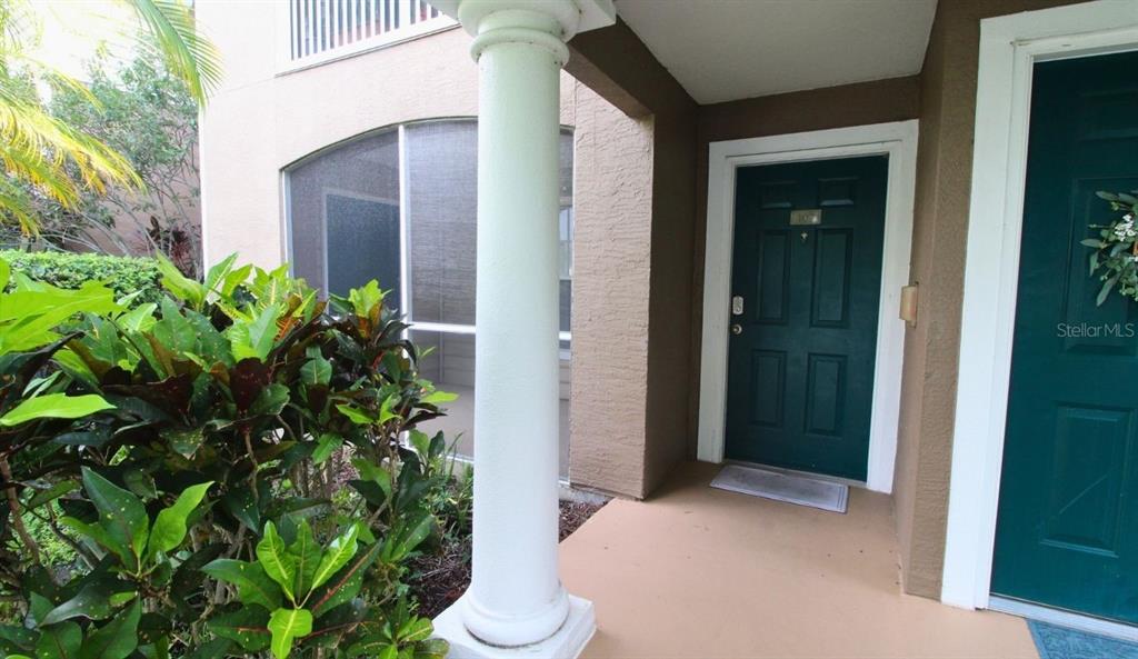A covered entryway features a white column, a dark green front door, and nearby landscaping — 8905 MANOR LOOP UNIT 107, BRADENTON, FL