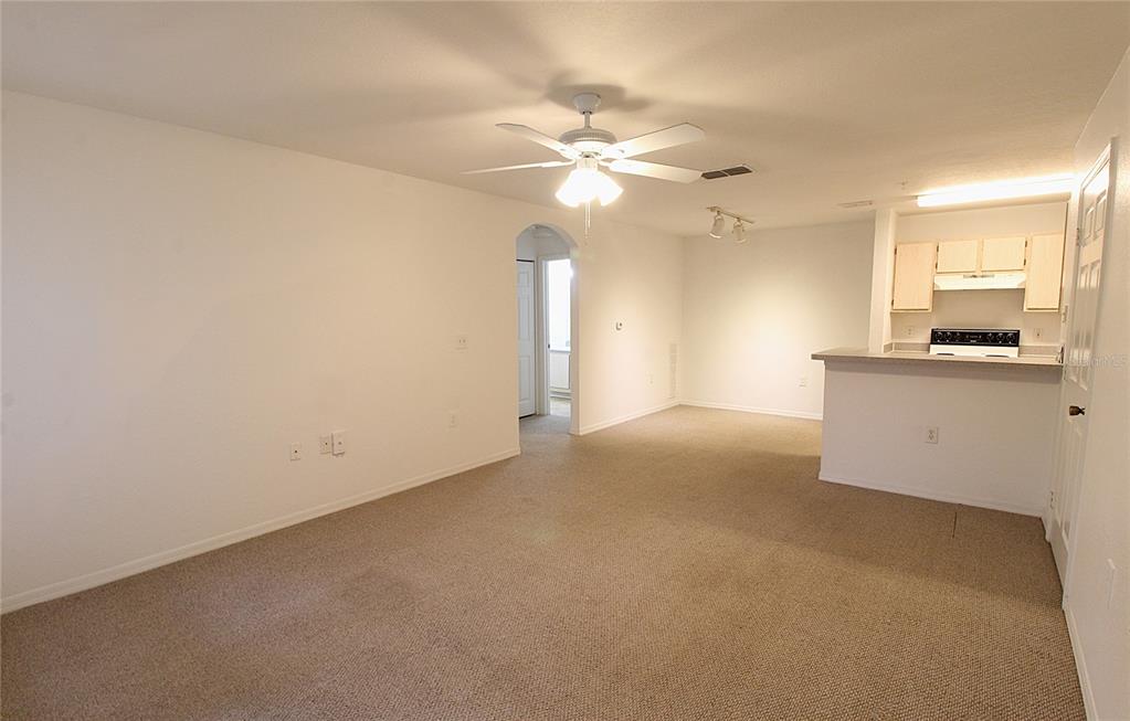 A carpeted living room features a ceiling fan and an open kitchen with white cabinets — 8905 MANOR LOOP UNIT 107, BRADENTON, FL