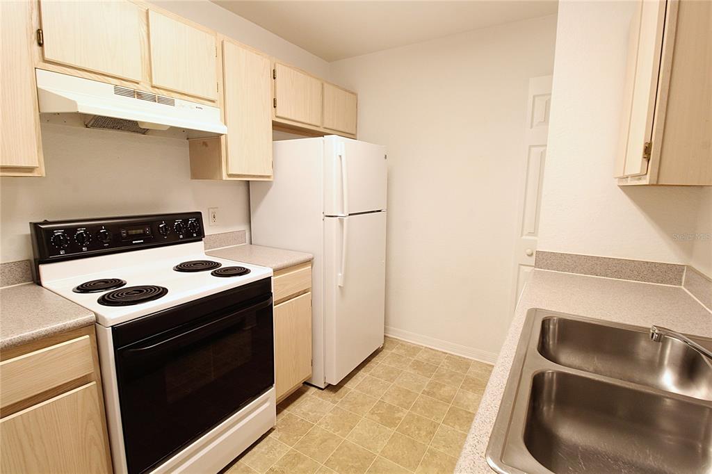 A kitchen features light wood cabinets, white appliances, laminate countertops, and a double-basin sink — 8905 MANOR LOOP UNIT 107, BRADENTON, FL