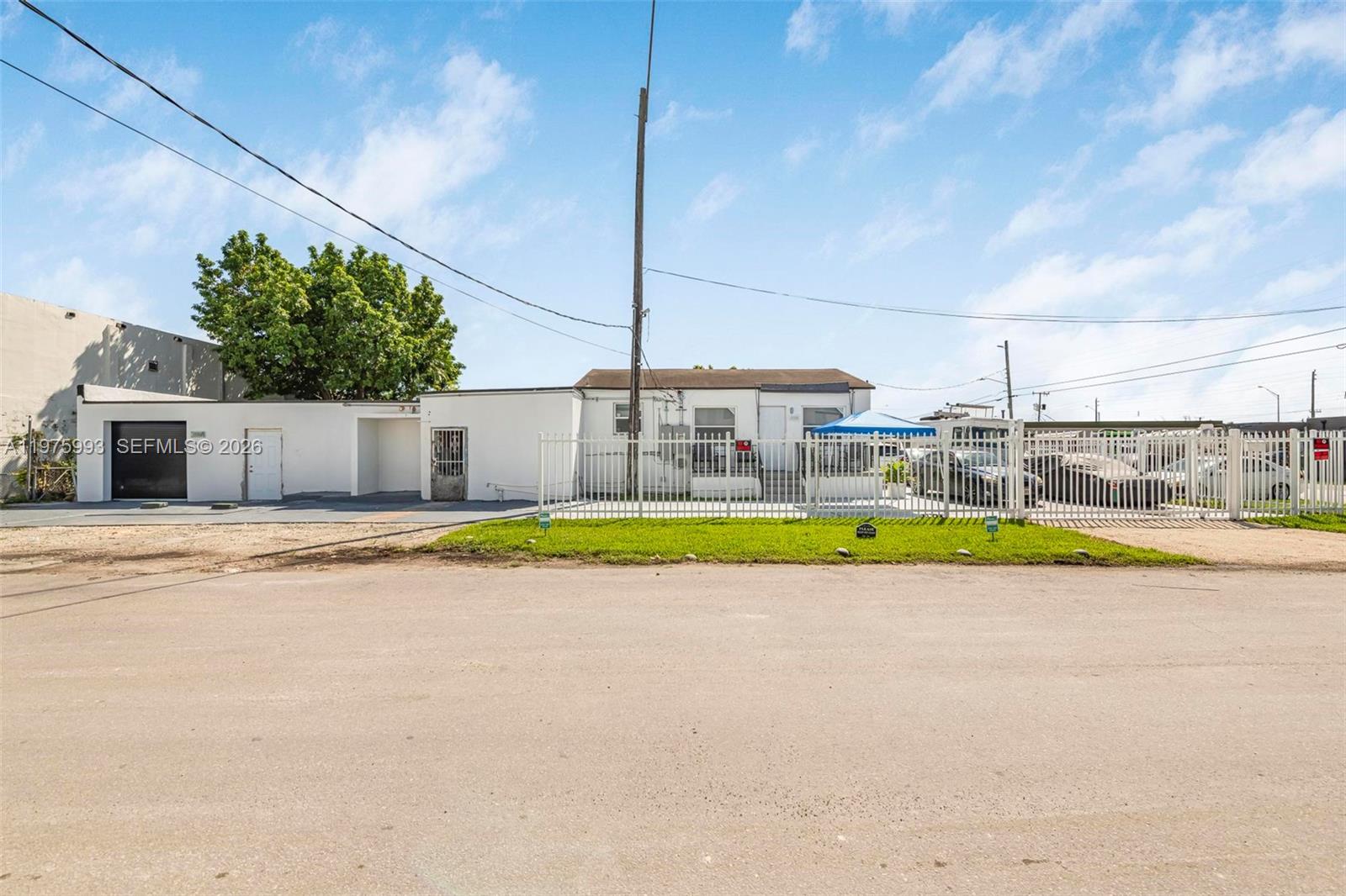 A single-story building with a white fence stands behind a dirt lot under a blue sky — 3705 NW 35th Ave, Miami FL 33142, MIAMI, FL