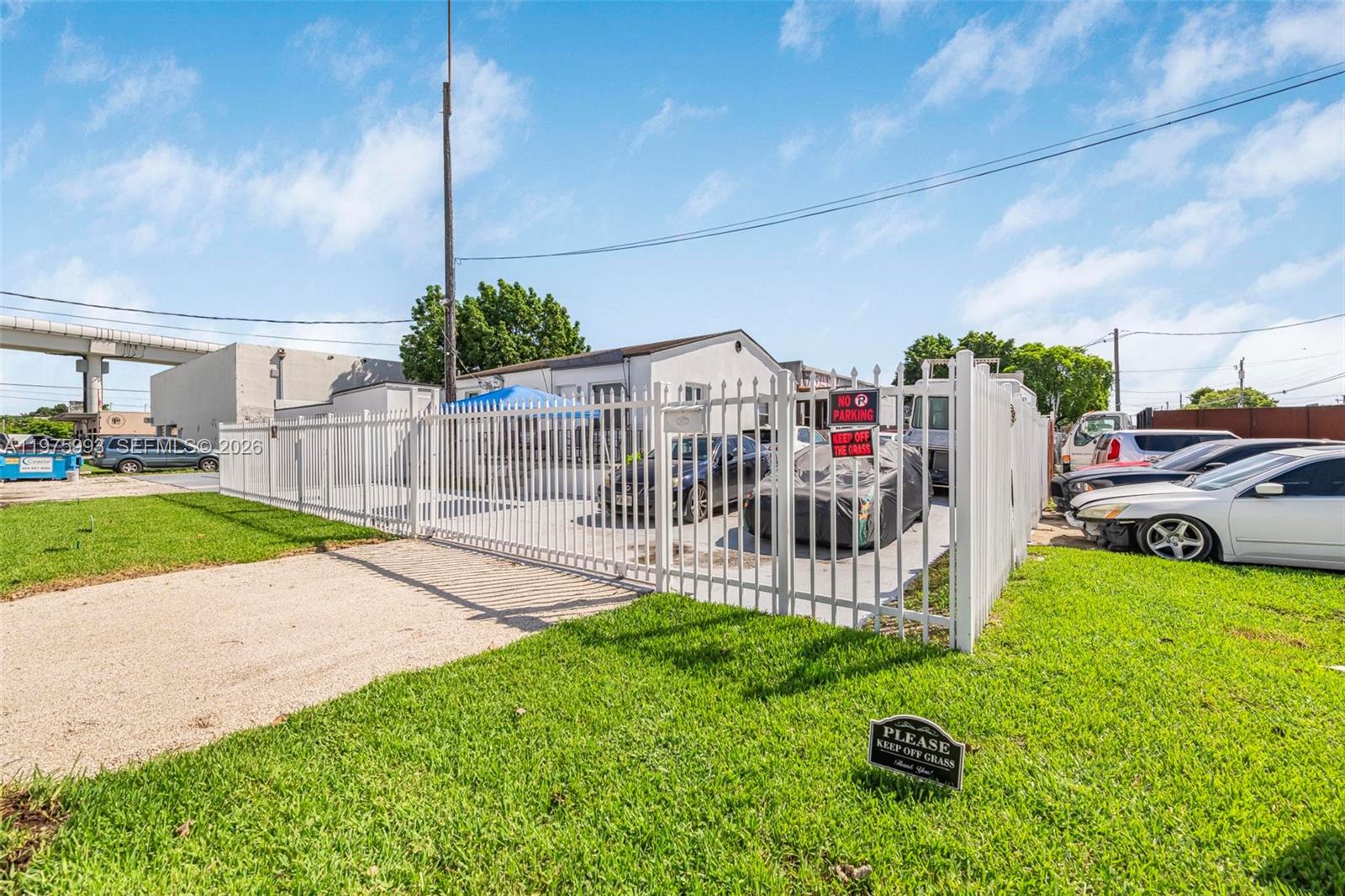 A white metal fence encloses a gravel parking area with several cars in front of a building — 3705 NW 35th Ave, Miami FL 33142, MIAMI, FL