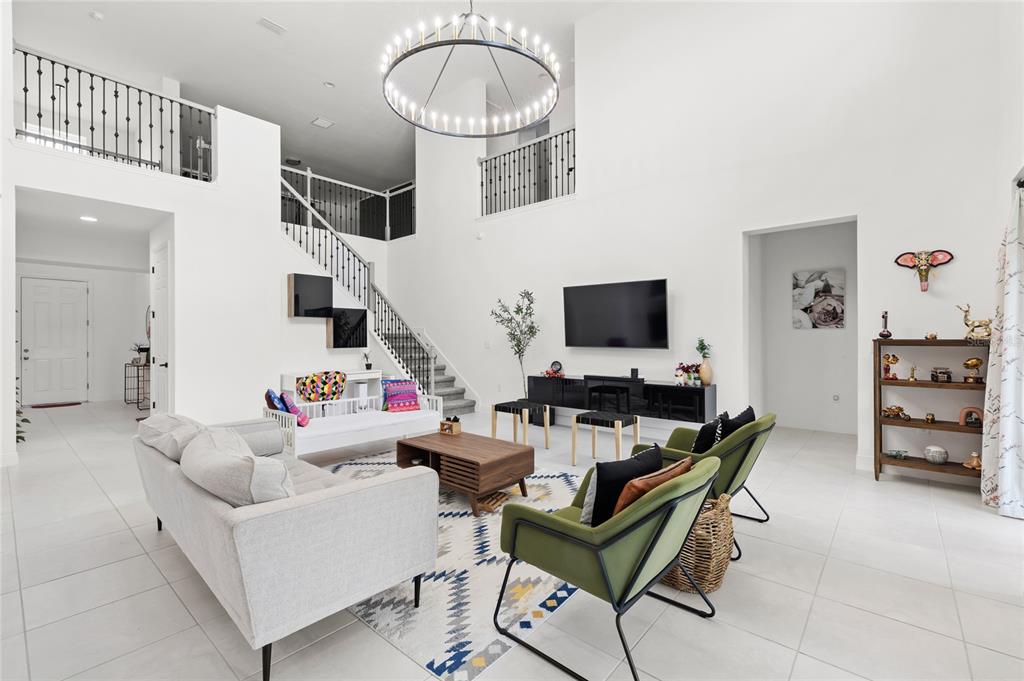 A spacious, high-ceilinged living room features white walls, tile flooring, a staircase, and modern furniture — 7647 MODICA STREET, CLERMONT, FL