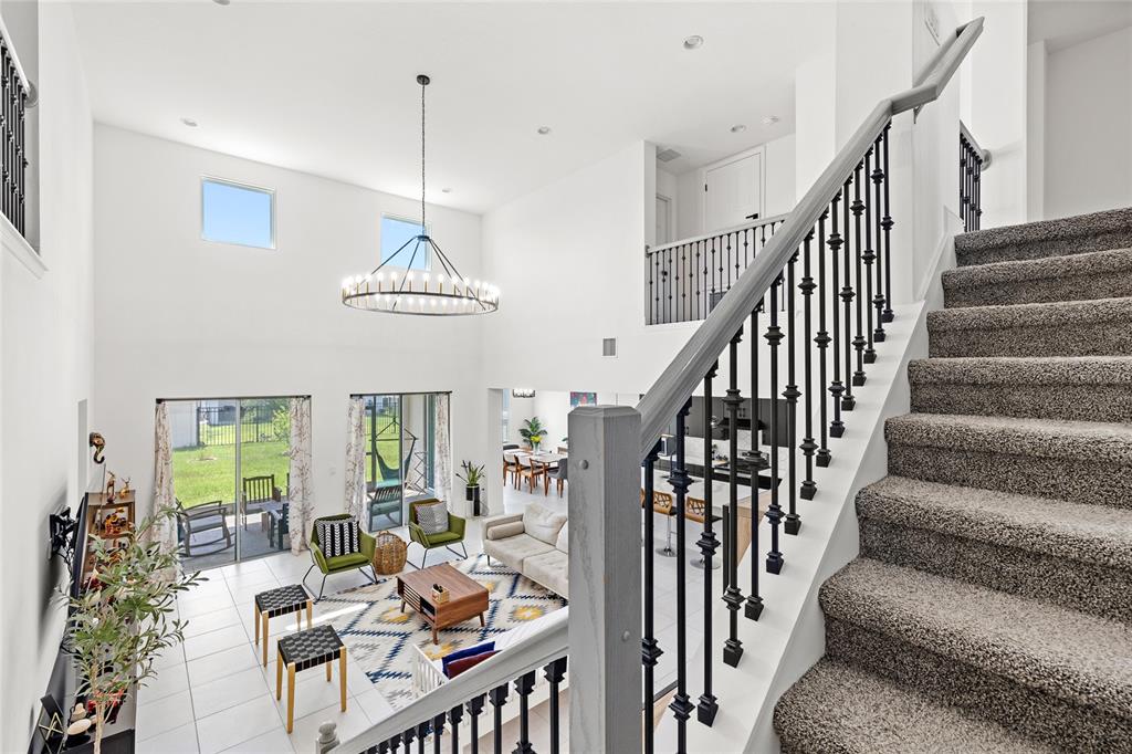 A high-ceilinged living room with a staircase, chandelier, and sliding doors to a backyard — 7647 MODICA STREET, CLERMONT, FL