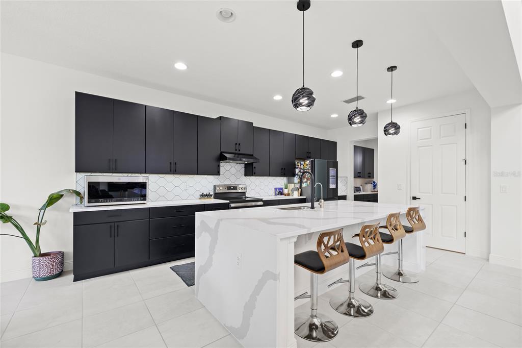A modern kitchen features black cabinetry, white quartz countertops, an island with barstools, and pendant lighting — 7647 MODICA STREET, CLERMONT, FL
