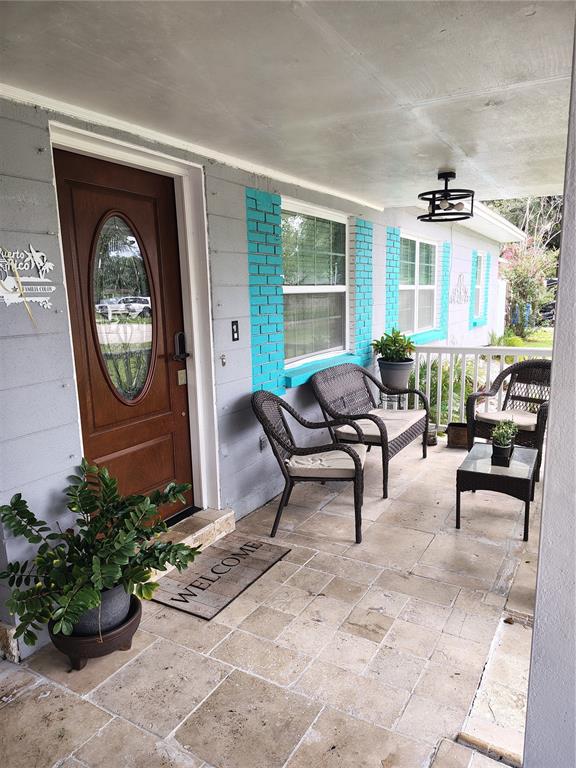 A covered front porch features stone tile flooring, wicker furniture, and bright turquoise window trim — 607 OAK RIDGE DRIVE, BRANDON, FL