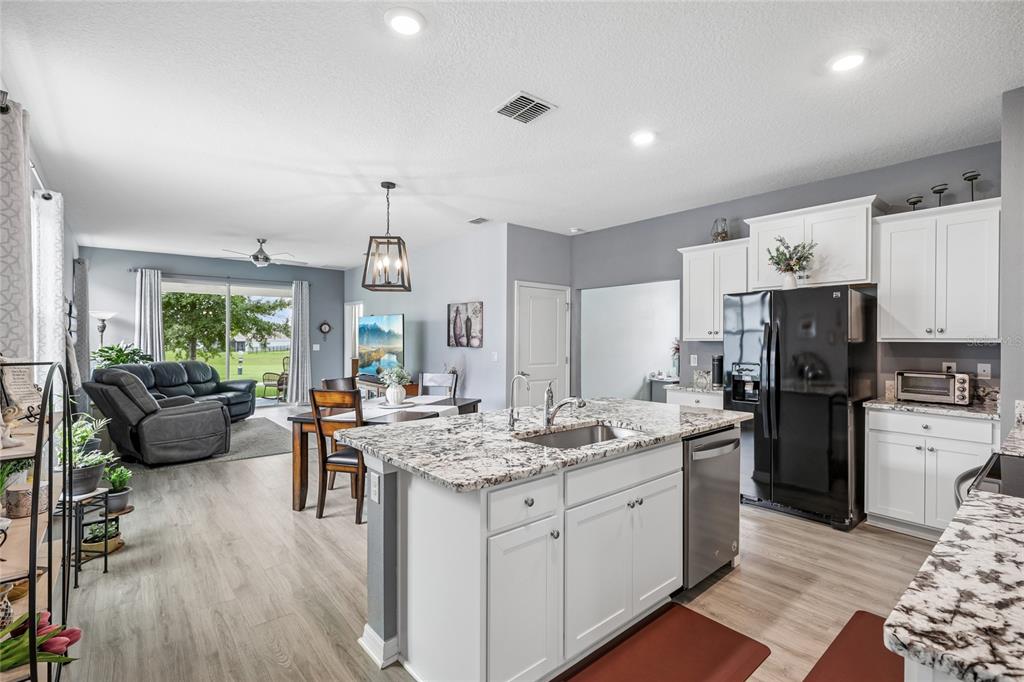 An open-concept kitchen with a granite island overlooks a dining area and living room — 5395 SUNSHINE DRIVE, WILDWOOD, FL