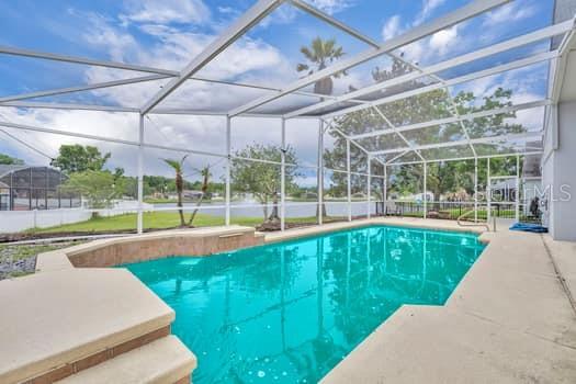 A screened-in swimming pool with a raised spa overlooks a lake and grassy yard — 1913 MAGIES COURT, OVIEDO, FL